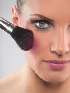 Close-up of young woman applying blush, studio shot