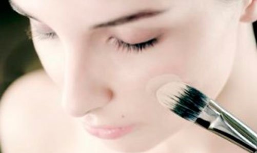 Young woman applying foundation to cheek with make-up brush, close-up